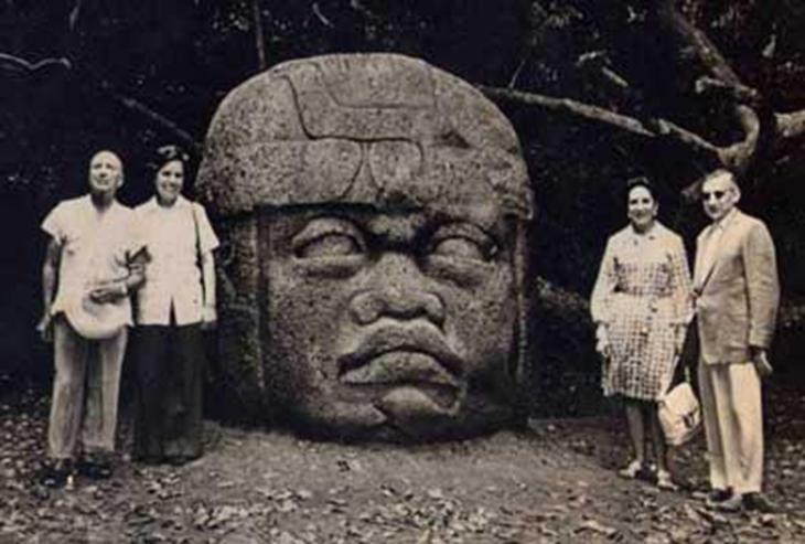 Casais de turistas posando ao lado de uma cabeça Olmeca. Créditos: autoria desconhecida. quatro pessoas ao lado de uma cabeça olmeca