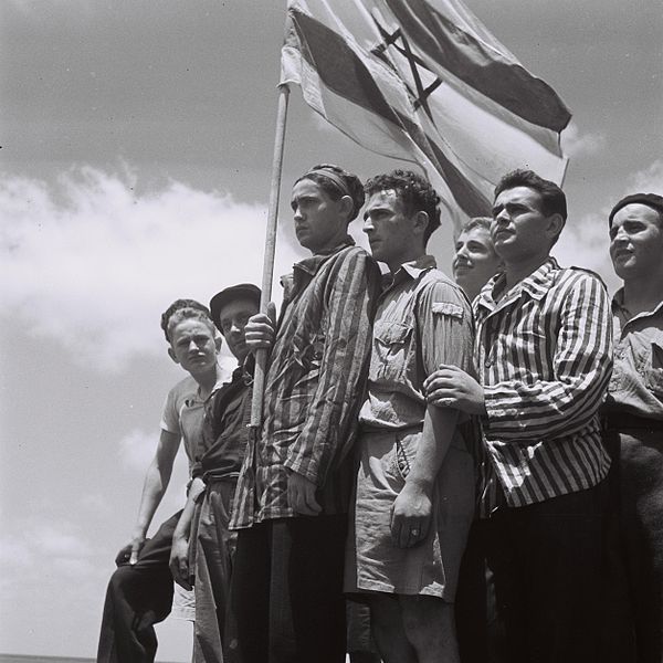 judeus com bandeira de Israel, alguns ainda com fardas de campo de concentração nazista, indo em direção à futura Israell